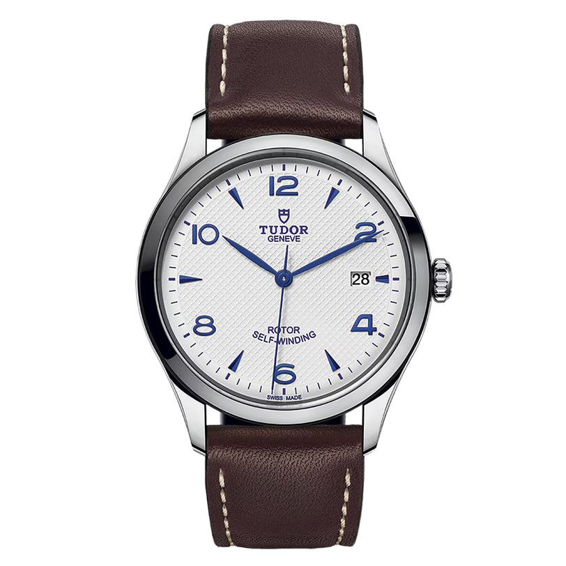 The TUDOR 1926 features a white textured dial with blue Arabic numerals, date at 3 o’clock, and a brown leather strap with white stitching—timeless elegance that embodies the classic appeal of TUDOR watches.