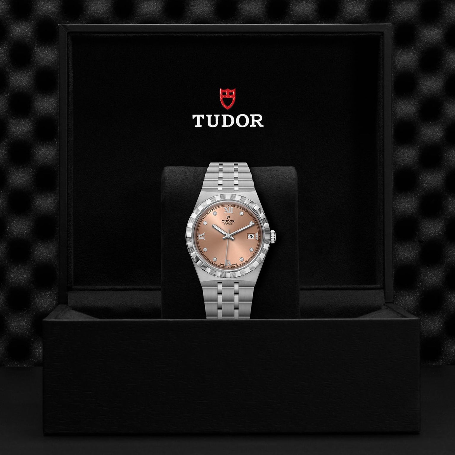 A TUDOR Royal wristwatch with a silver case and salmon dial displayed in an open black TUDOR box.