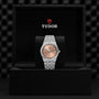 A TUDOR Royal wristwatch with a silver case and salmon dial displayed in an open black TUDOR box.