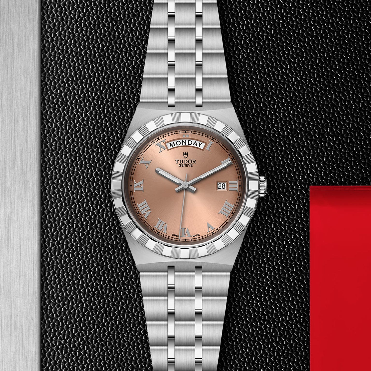 A TUDOR Royal stainless steel wristwatch with a salmon-tone dial, Roman numerals, automatic movement, and day-date display shown on a textured black background.