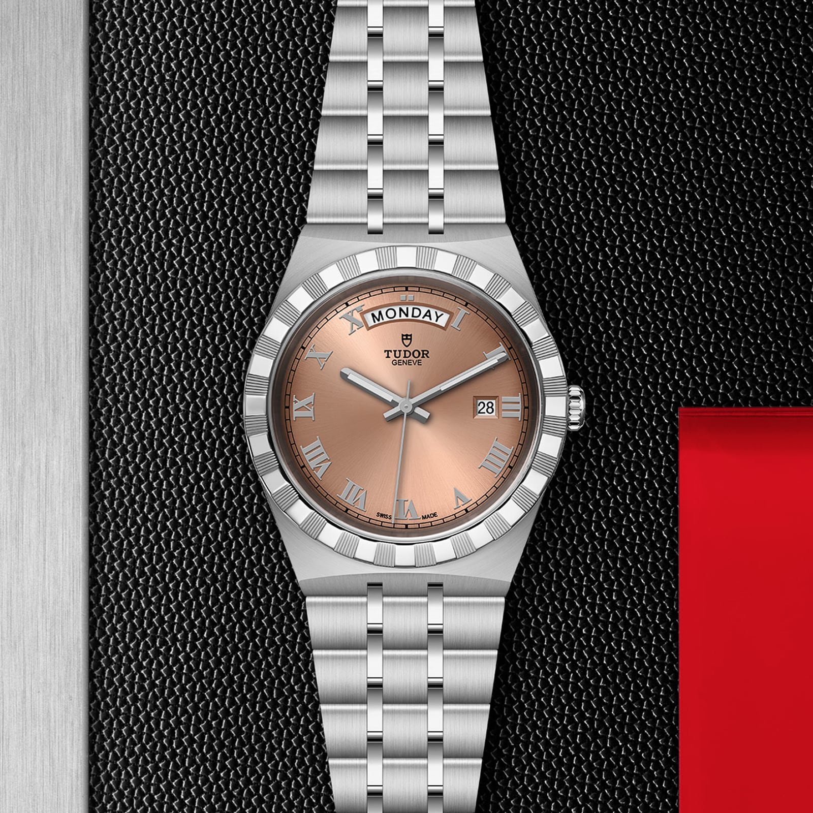 A TUDOR Royal stainless steel wristwatch with a salmon-tone dial, Roman numerals, automatic movement, and day-date display shown on a textured black background.