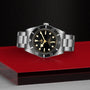 The TUDOR Black Bay 54 wristwatch with a black dial and bezel is displayed on a glossy red and black surface.