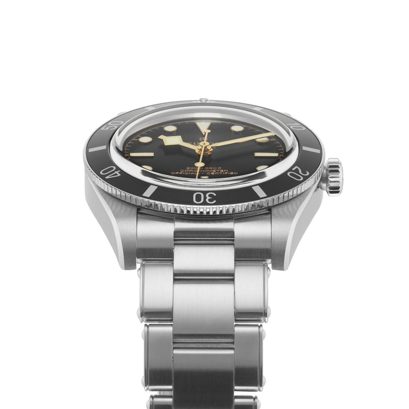 The TUDOR Black Bay 54 wristwatch features a black dial, metal band, and prominent hour markers, shown from an angle.