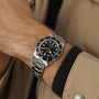 Someone wearing a beige jacket and a TUDOR Black Bay 54 watch with a black dial and bezel, featuring the Manufacture Calibre MT5400, on their wrist.
