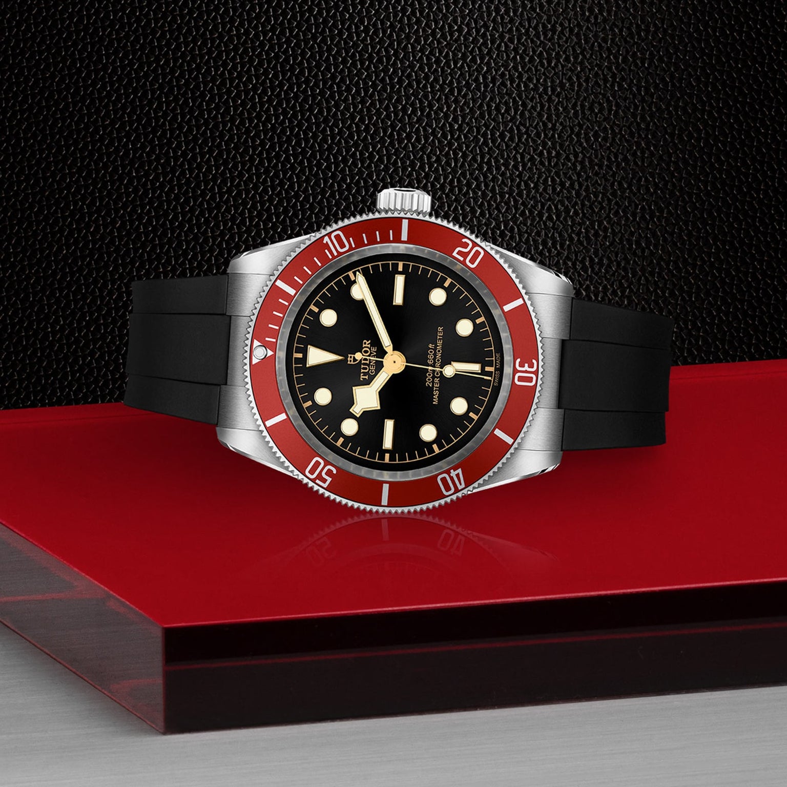 The TUDOR Black Bay wristwatch, featuring a burgundy bezel, black dial, and black rubber strap, is showcased on a red and black textured surface.