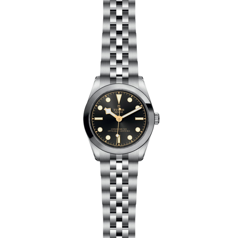 The TUDOR Black Bay 31 is a stainless steel unisex wristwatch with a black dial, round markers, and a five-link bracelet. It features Manufacture Calibres for precision and chic style, displayed against a white background.