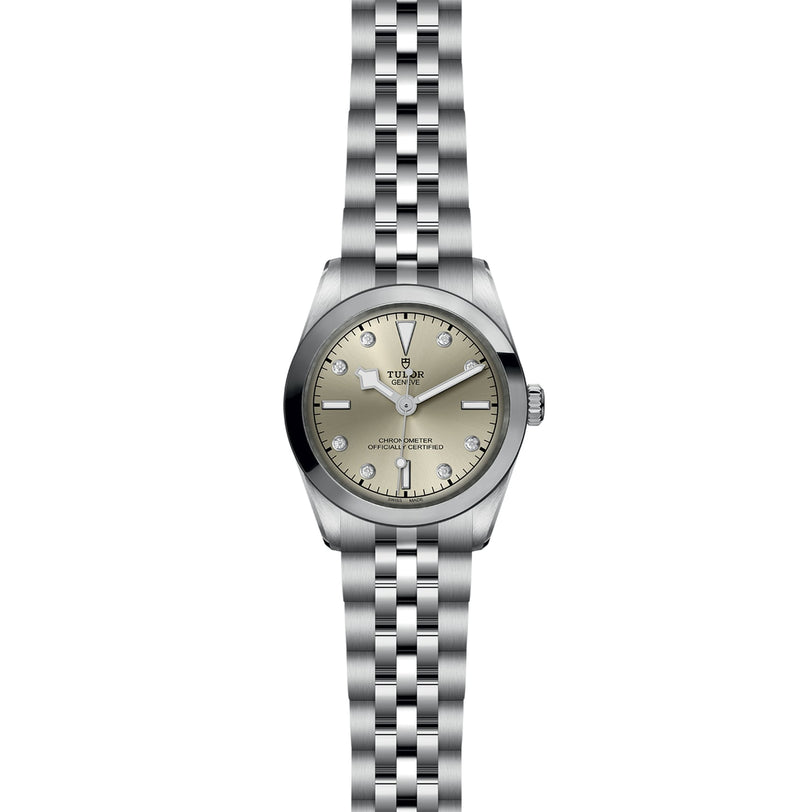 The TUDOR Black Bay One 31 wristwatch features a metal link band, light champagne dial, silver hour markers, and a date window at 3 o’clock; this unisex watch showcases refined watchmaking and is pictured from above on a white background.