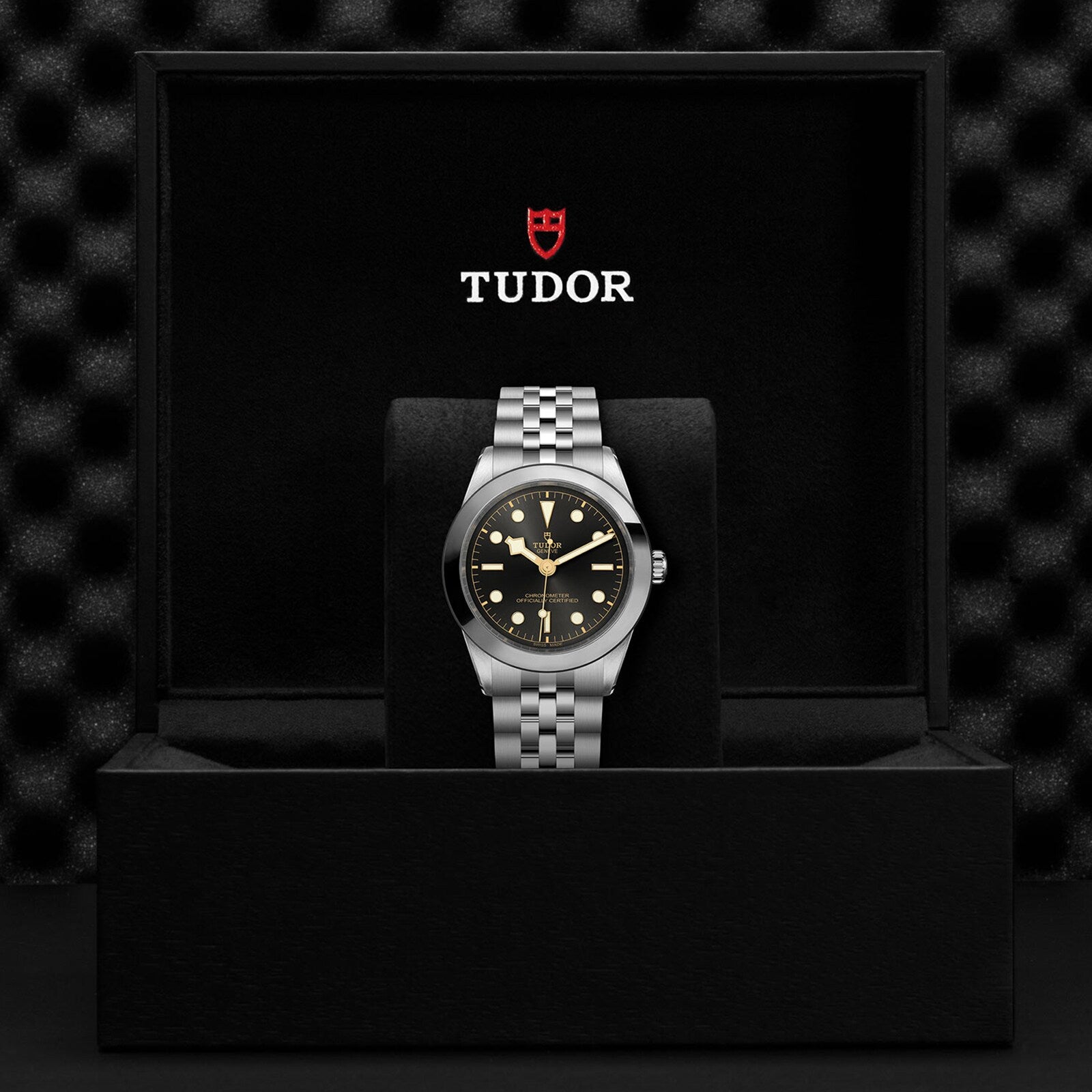 A TUDOR Black Bay One 39 wristwatch with a black dial and metal bracelet is displayed in an open black TUDOR box, highlighting its unisex style and precision Manufacture Calibre.