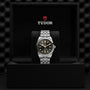 The TUDOR Black Bay One 41 wristwatch features a black and gold dial on a silver 316L steel bracelet, presented in an open black TUDOR box with logo—a unisex statement of chic style.