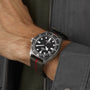 A person wearing a TUDOR Pelagos FXD diving watch with a black bezel and a green fabric strap accented by a red stripe.