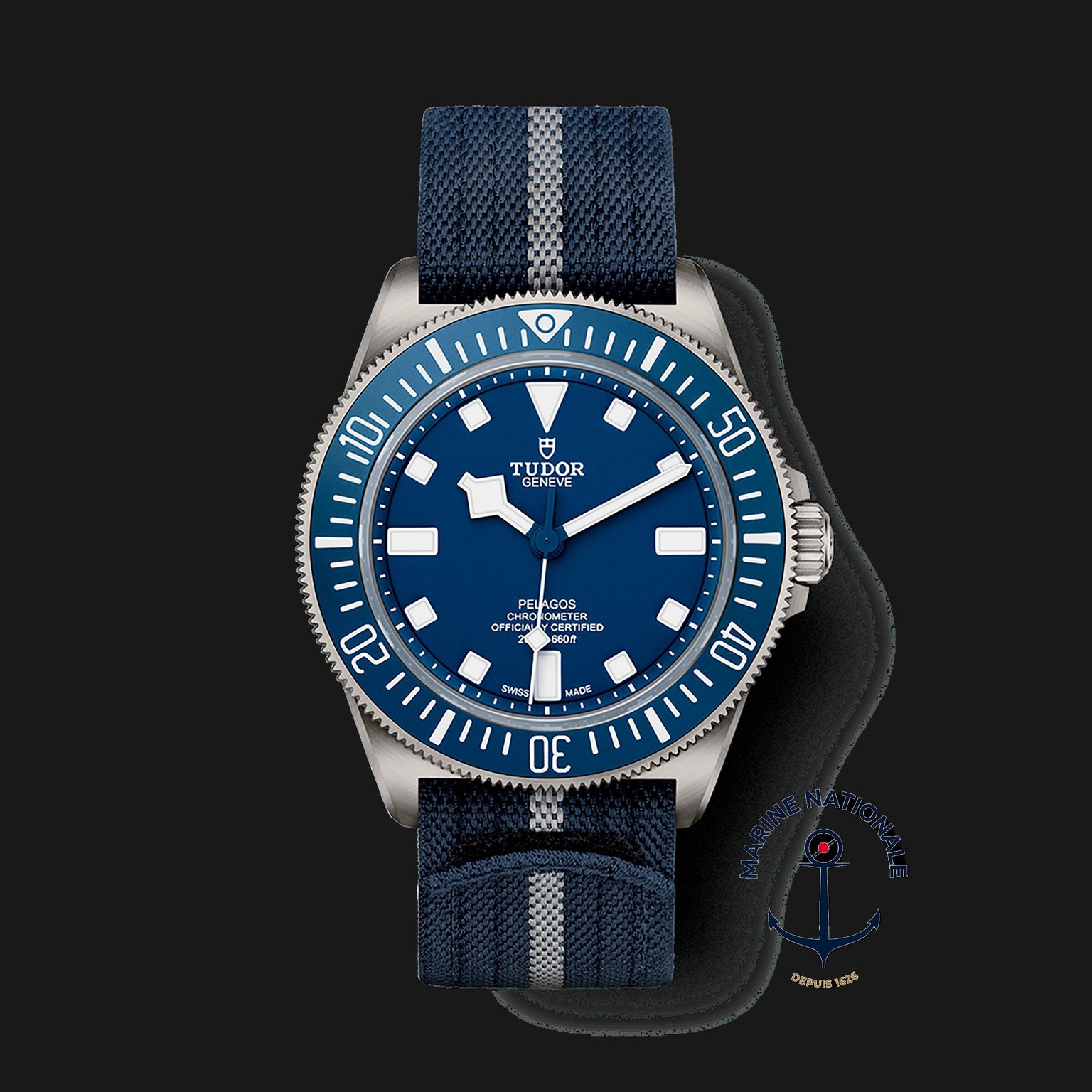 The TUDOR Pelagos FXD features a blue dial and bezel, a blue fabric strap with grey stripe, and a Marine Nationale emblem—making it a distinctive modern diver’s watch.