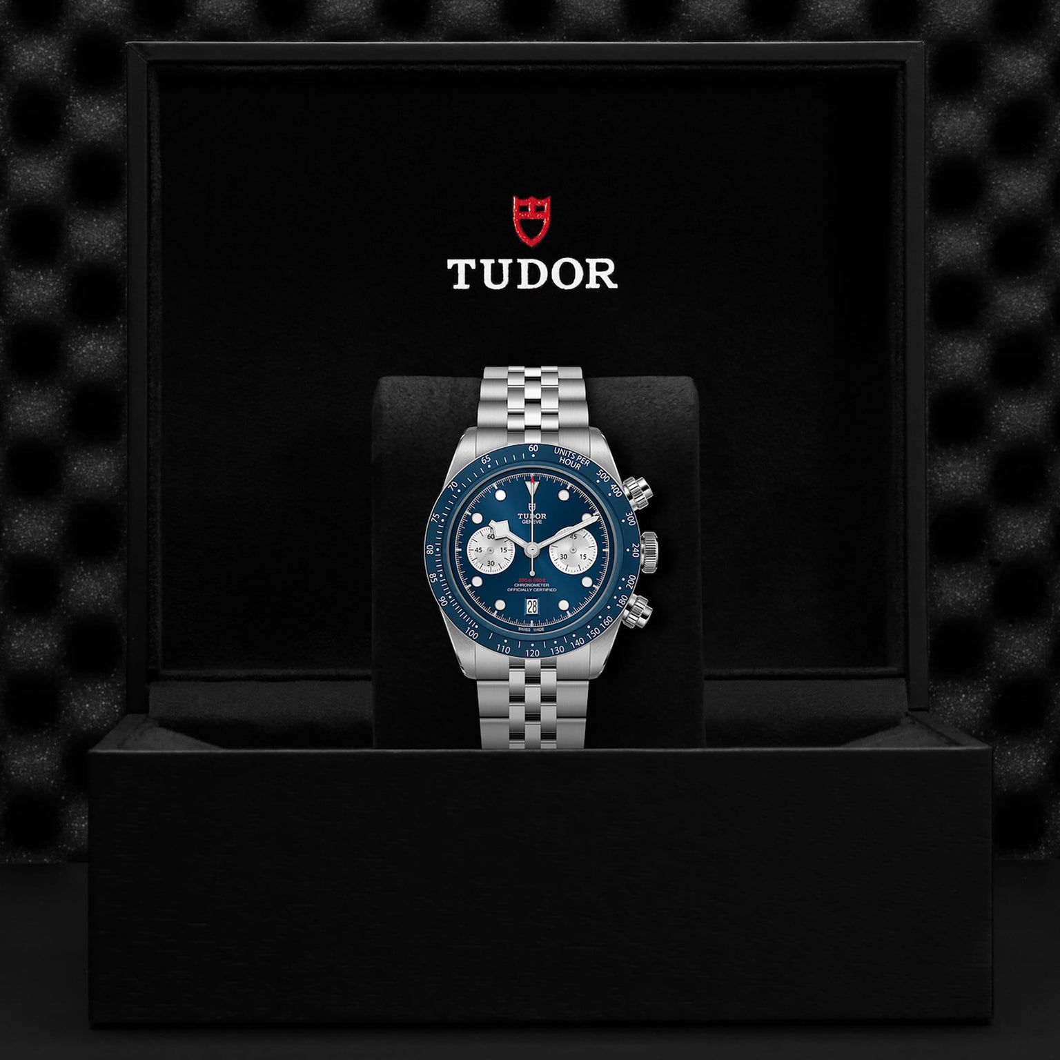 A TUDOR Black Bay Chrono wristwatch with a blue dial and silver bracelet stands upright in an open black presentation box featuring the TUDOR logo, as seen in select Tudor Boutiques.