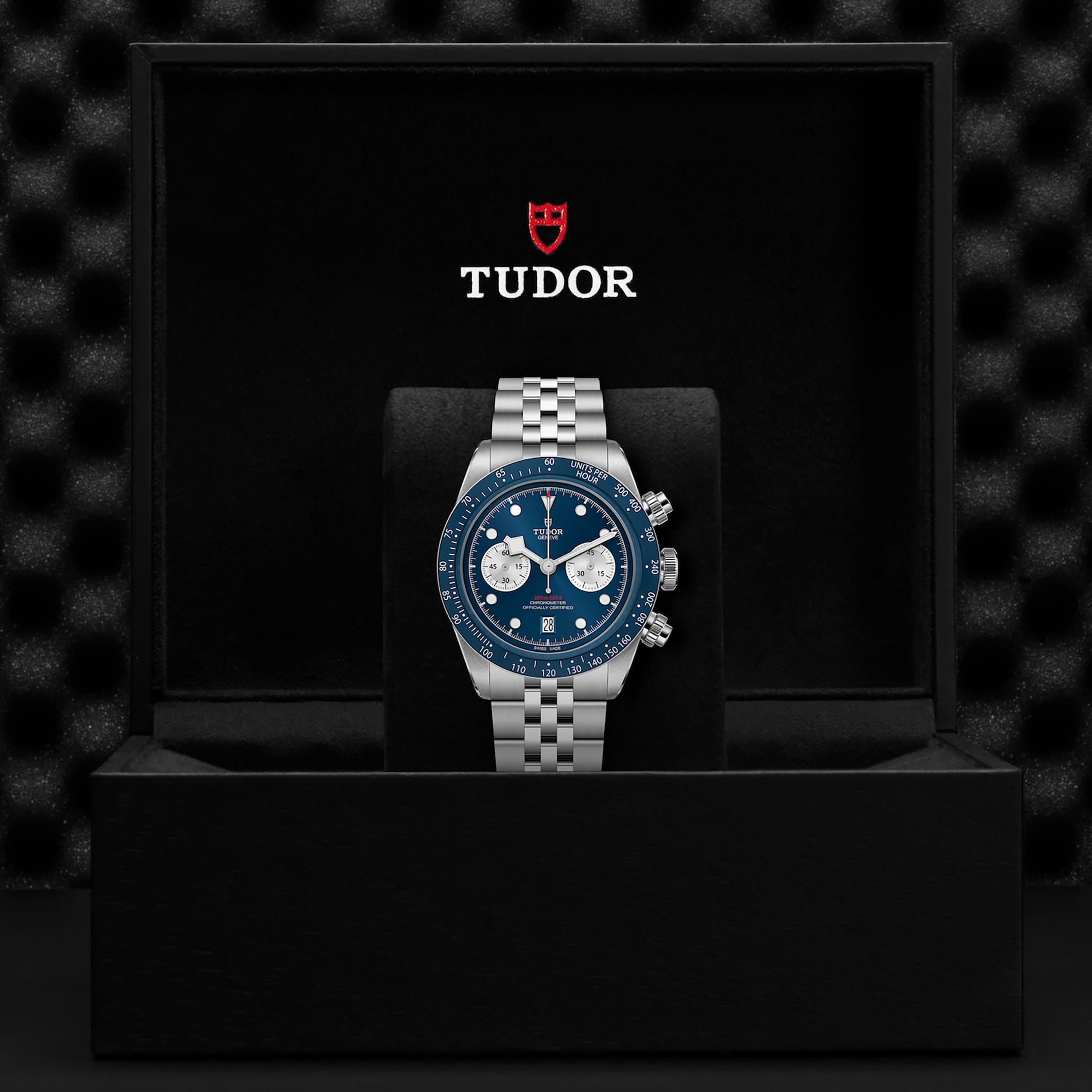 A TUDOR Black Bay Chrono wristwatch with a blue dial and silver bracelet stands upright in an open black presentation box featuring the TUDOR logo, as seen in select Tudor Boutiques.