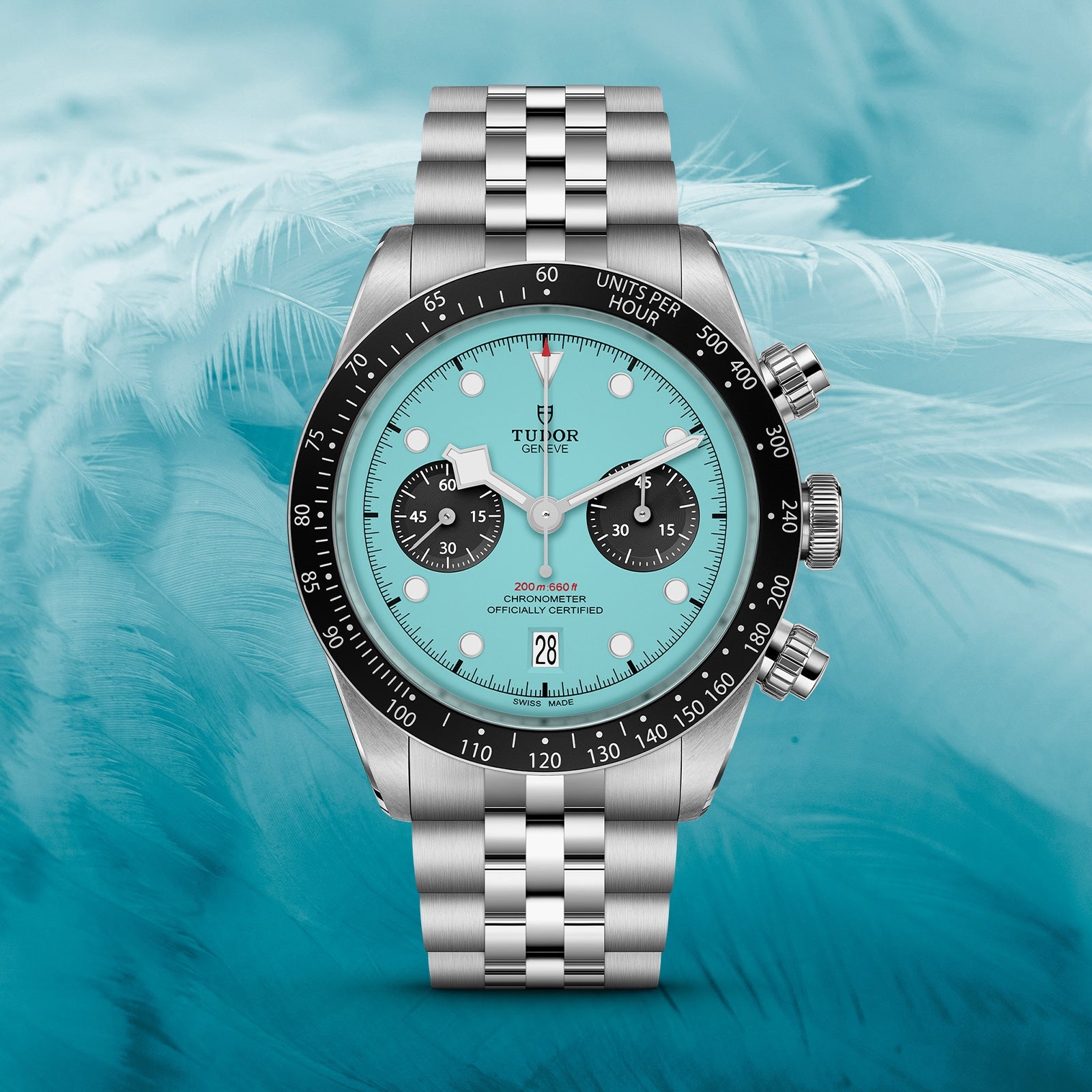The TUDOR Black Bay Chrono with a turquoise dial, black bezel, and jubilee bracelet is displayed against a light blue feather background, highlighting its Swiss Chronometer precision.