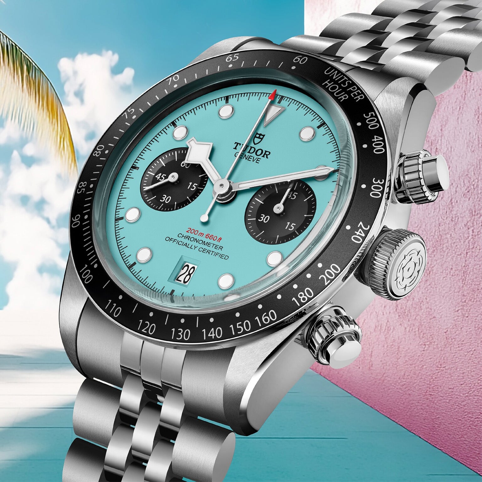 The TUDOR Black Bay Chrono with a turquoise dial and black subdials is showcased against a pastel backdrop featuring a palm tree and pink wall, emphasizing its Swiss Chronometer precision.