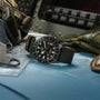 The TUDOR Pelagos FXD GMT, featuring a green strap, is displayed on a map surrounded by flight gear and cockpit controls.