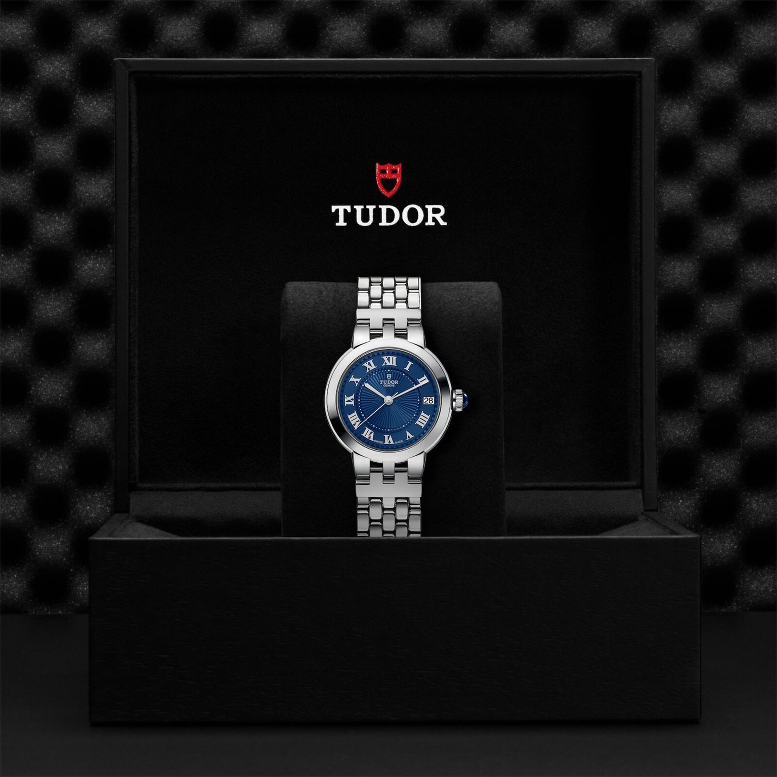 A TUDOR Clair de Rose silver wristwatch with a blue face, presented in a black box featuring the TUDOR logo.