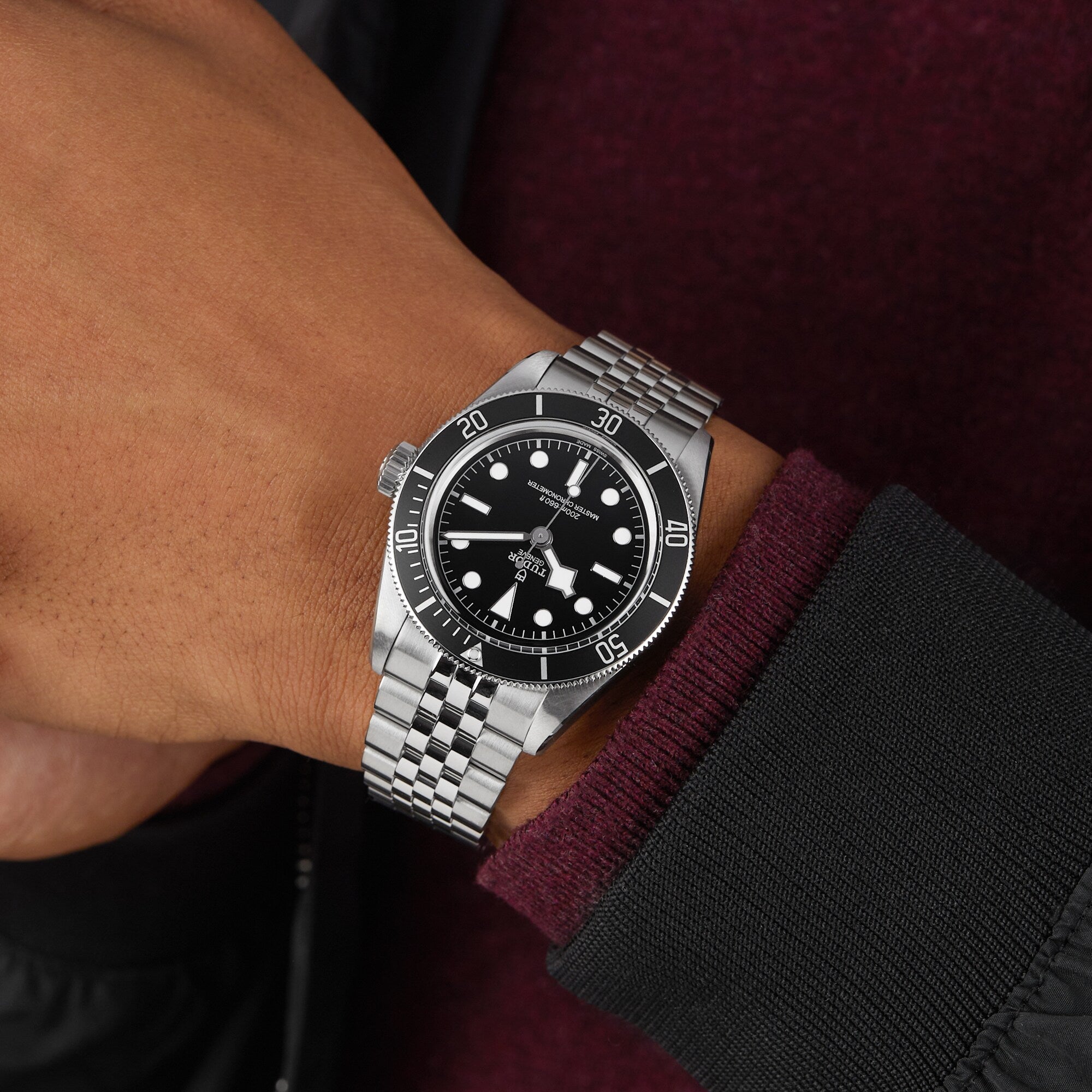A person wearing a TUDOR Black Bay watch with a stainless steel bracelet and black bezel on their left wrist.