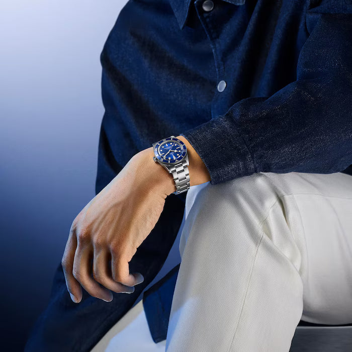 Steel watch with blue dial and rotating bezel on metal bracelet worn on wrist.