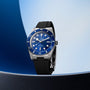 Tudor Black Bay 54 watch with blue dial, silver case, and black rubber strap on blue background.