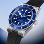 Tudor watch with stainless steel case, blue dial, blue rotating bezel, and black rubber strap.