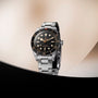 Steel dive watch with black dial, luminous hour markers, rotating bezel, and steel bracelet on neutral background.