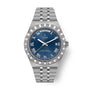 Stainless steel watch with blue dial, Roman numerals, day-date window, and textured bezel on matching bracelet.