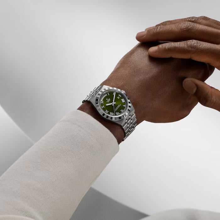 Stainless steel watch with green dial and chronograph subdials worn on wrist.