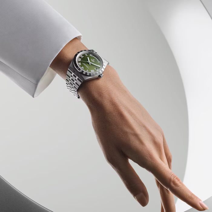 Stainless steel watch with green dial and matching bracelet worn on wrist with white dress shirt.