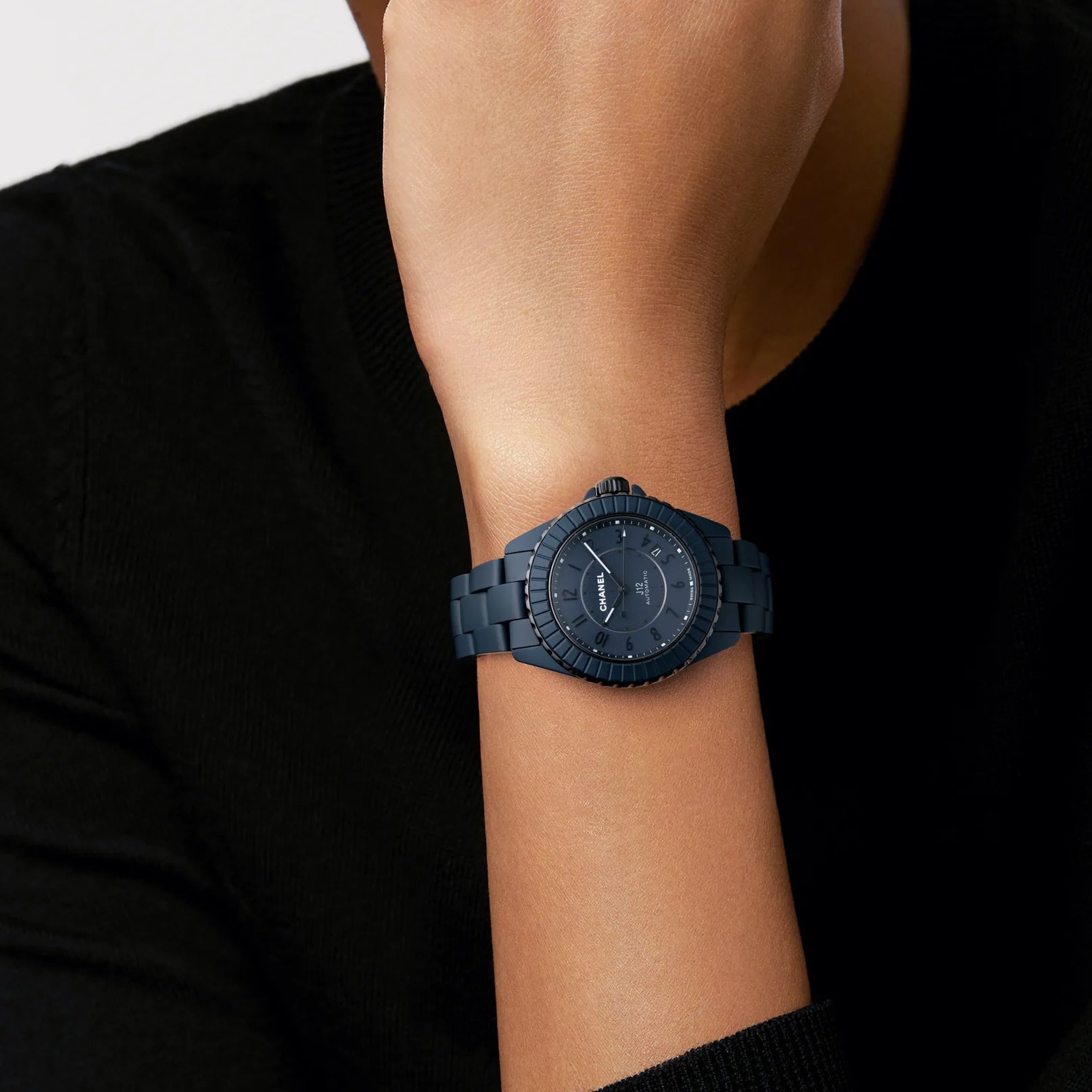 A person wearing the Chanel J12 Bleu Watch Caliber 12.1, 38 mm, with a black metal band and bezel, rests their hand on their chin.
