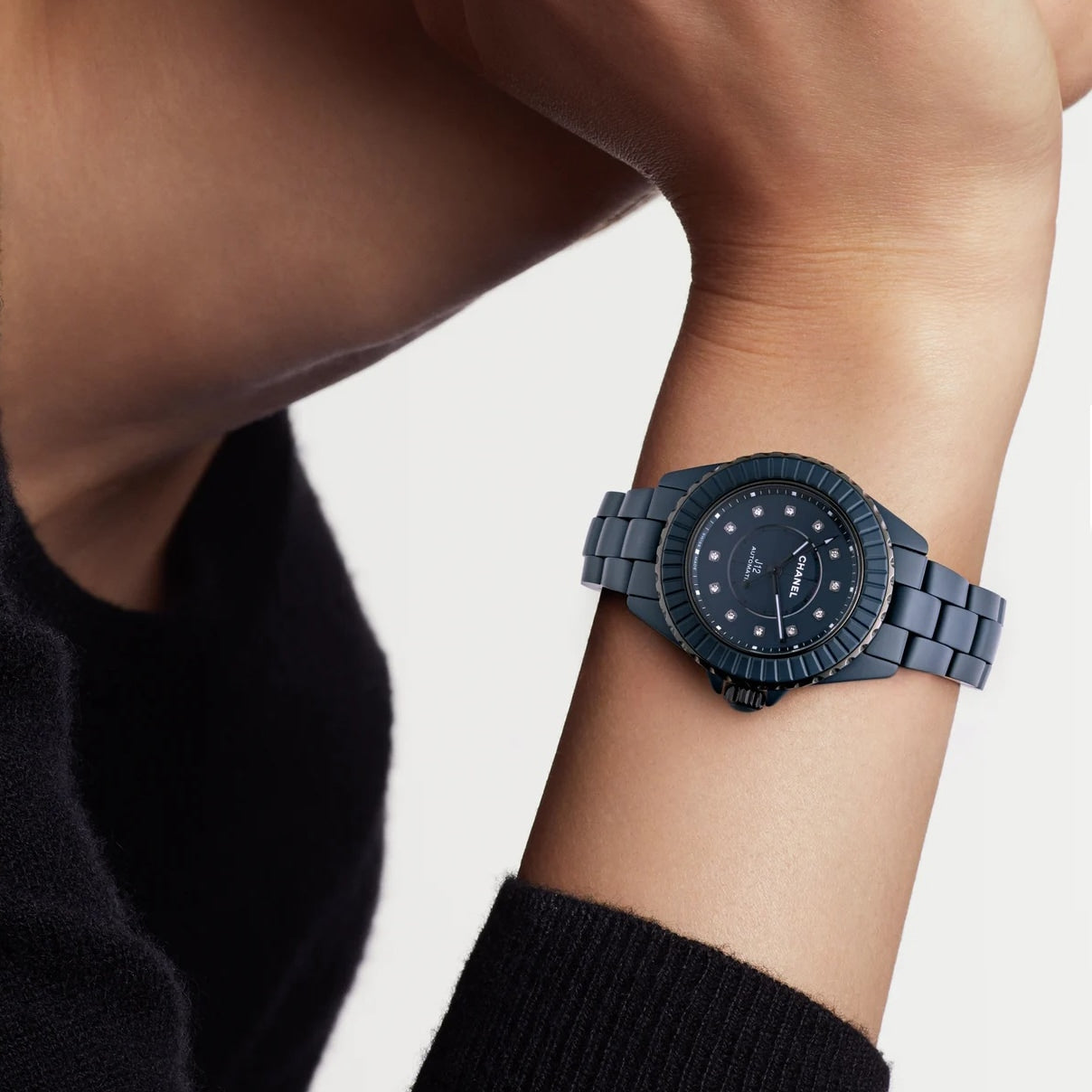 A person wearing a Chanel J12 Bleu Watch Caliber 12.2, 33 mm with a dark blue round face and metallic strap on their left wrist.