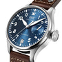 A close-up of the IWC Schaffhausen Big Pilots Watch Edition Le Petit Prince shows its automatic movement, blue dial, date window, power reserve indicator, stainless steel case, and brown leather strap.