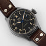 A close-up of the IWC Schaffhausen Big Pilots Watch Heritage shows its automatic movement, black dial, brown leather strap, blue power reserve hand, and a date display at 6 oclock.