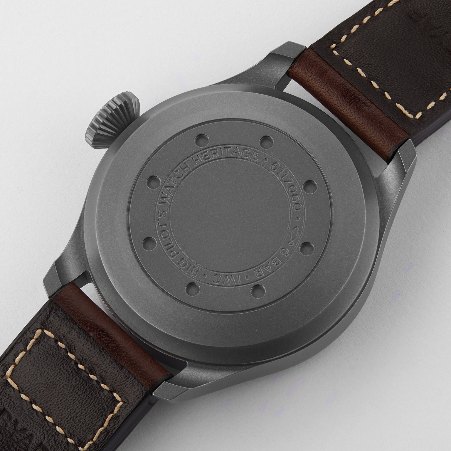 A close-up of the back of the IWC Schaffhausen Big Pilots Watch Heritage features its matte gray titanium case and brown leather strap, with engraved text—an elegant tribute to classic pilot’s watches.