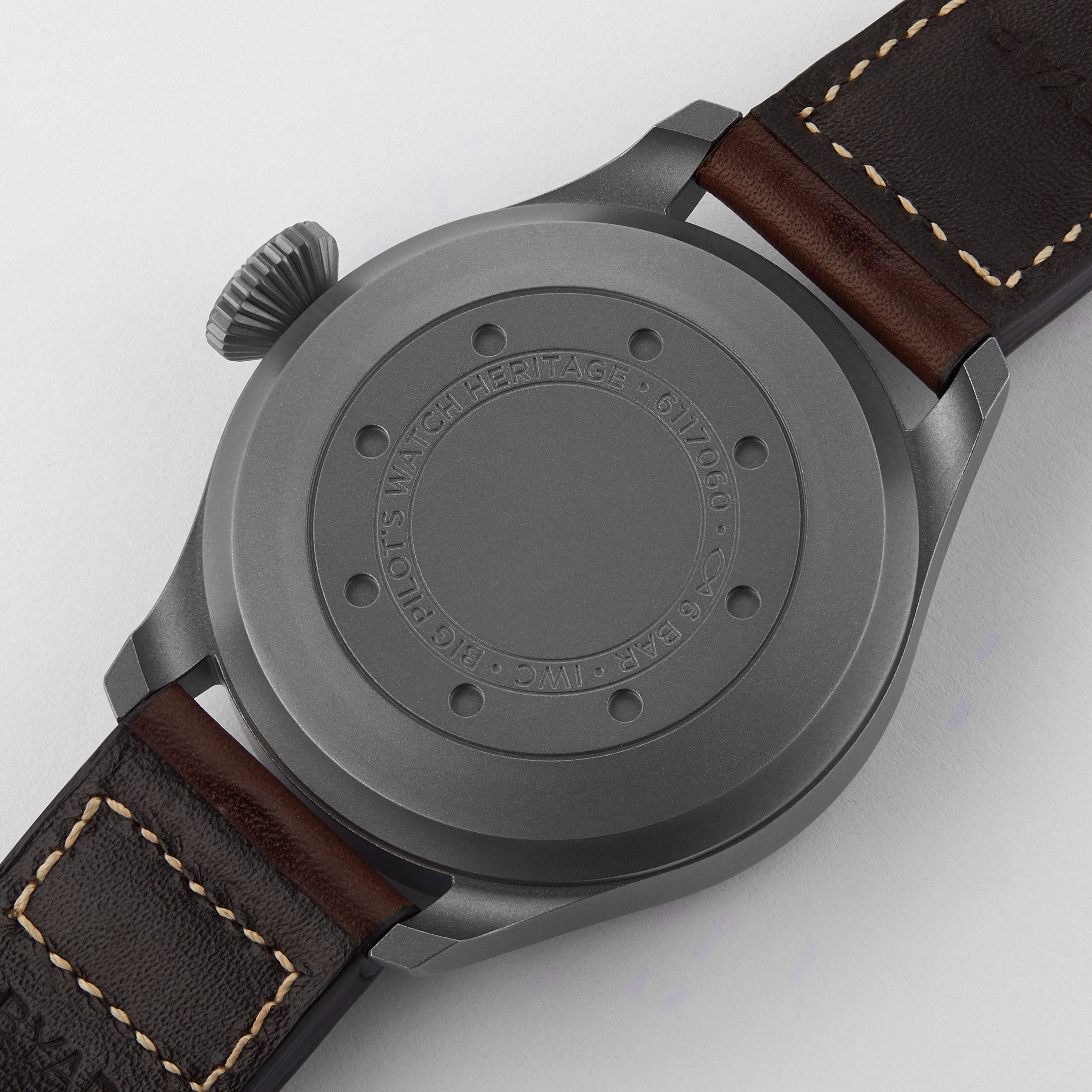 A close-up of the back of the IWC Schaffhausen Big Pilots Watch Heritage features its matte gray titanium case and brown leather strap, with engraved text—an elegant tribute to classic pilot’s watches.