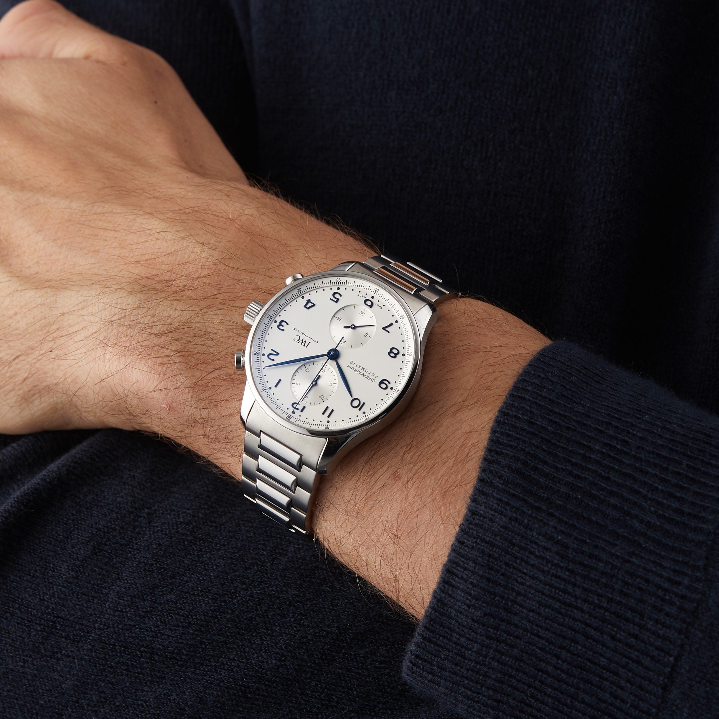 A person in a dark long-sleeve shirt wears an IWC Schaffhausen Portugieser Chronograph featuring a white dial, black numerals, and a stainless steel bracelet.
