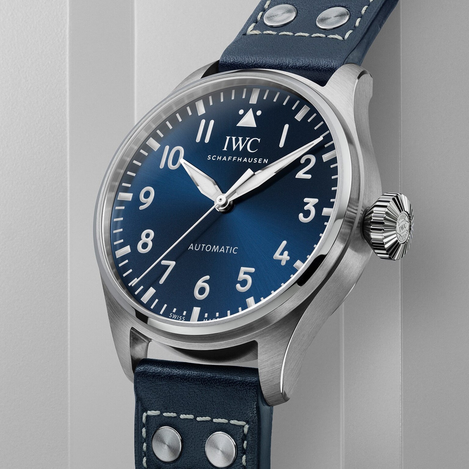 A close-up of the IWC Schaffhausen Big Pilots Watch 43, showcasing its striking blue dial, white numerals, and a blue leather strap with crisp white stitching and rivets—a true pilot’s watch icon.