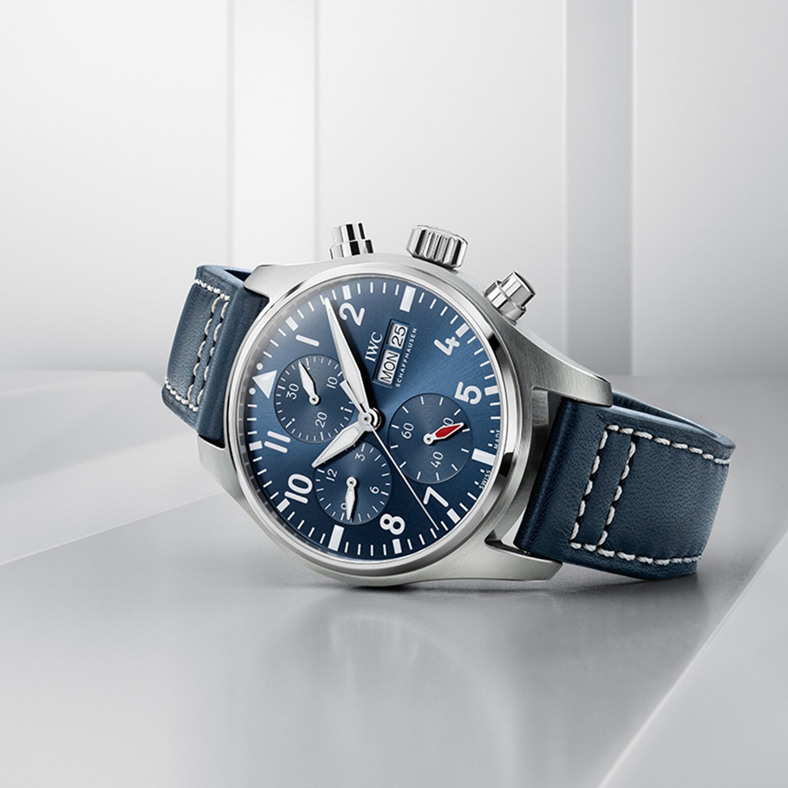 The IWC Schaffhausen Pilots Watch Chronograph 41 features a stainless steel case, blue dial with white numerals, and a matching blue leather strap, showcased against a white geometric background.