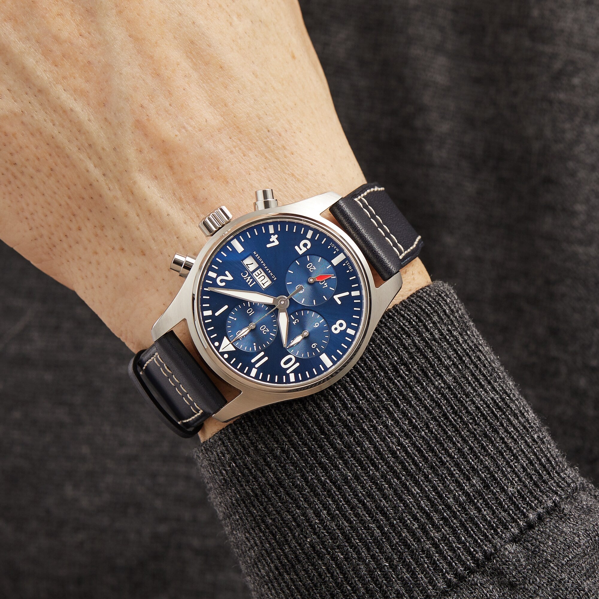 An IWC Schaffhausen Pilots Watch Chronograph 41, featuring a blue dial with three subdials and a black leather strap, worn over a dark long-sleeve sweater.