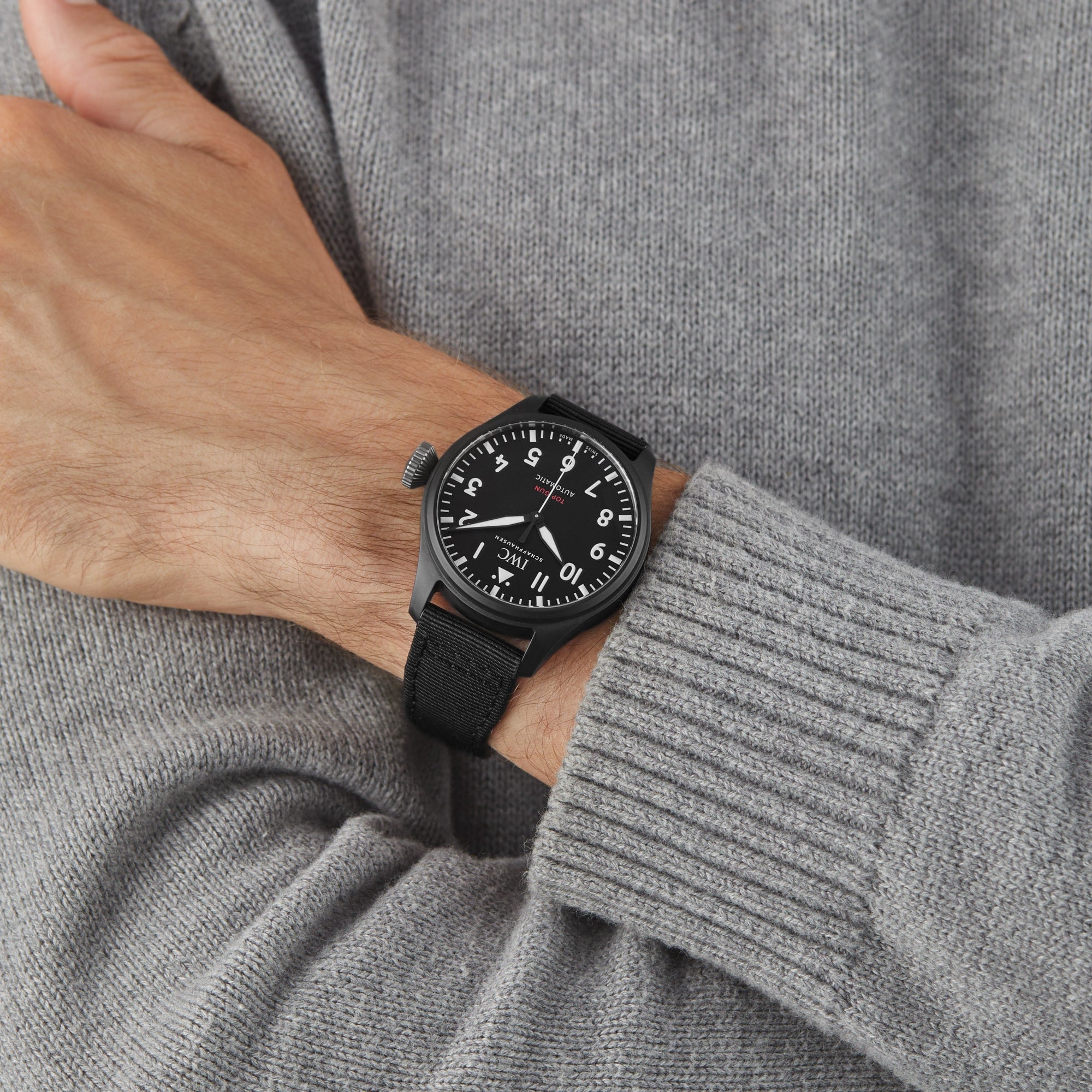 Someone wears an IWC Schaffhausen Big Pilots Watch 43 Top Gun with a black ceramic case and black strap, paired with a light grey knit sweater.
