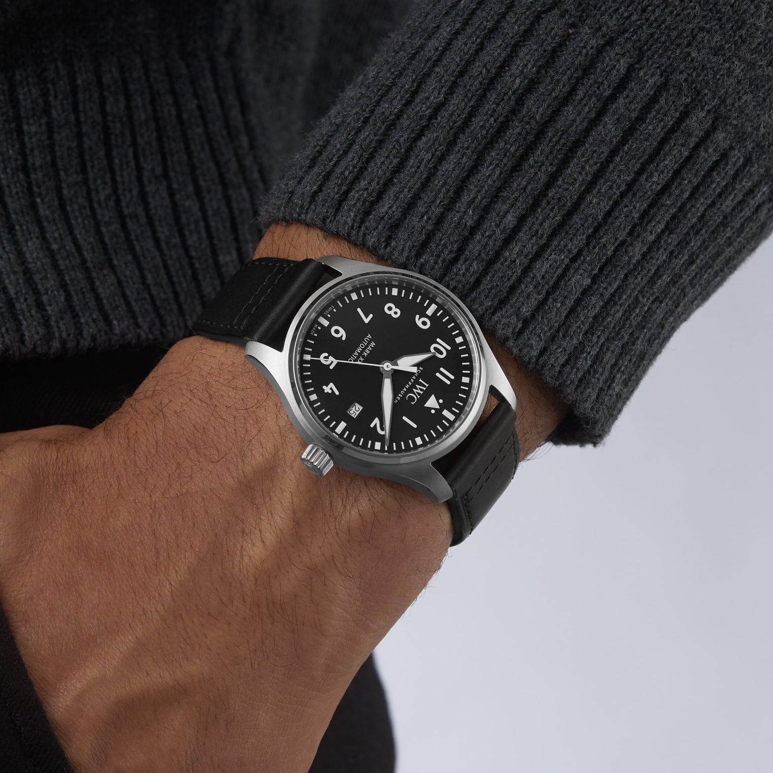 A person wearing the IWC Schaffhausen Pilots Watch Mark XX with a black strap, white numerals, and stainless steel case, styled with a dark grey ribbed sweater.