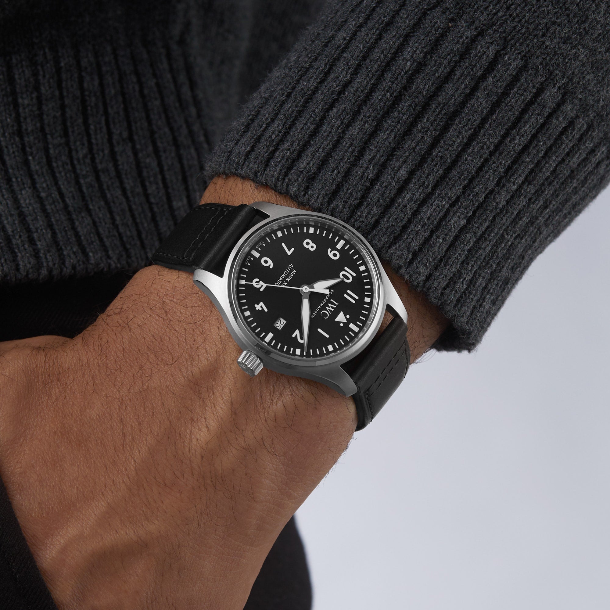 A person wearing the IWC Schaffhausen Pilots Watch Mark XX with a black strap, white numerals, and stainless steel case, styled with a dark grey ribbed sweater.