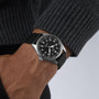 A person wearing the IWC Schaffhausen Pilots Watch Mark XX with a black strap, white numerals, and stainless steel case, styled with a dark grey ribbed sweater.