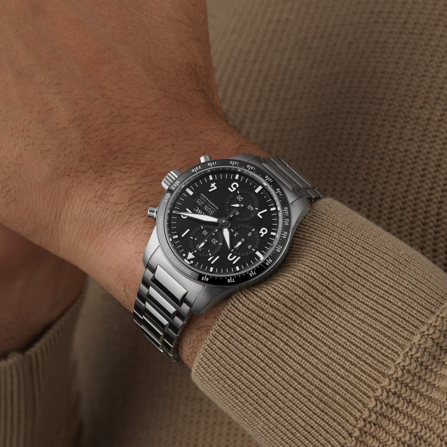 An IWC Schaffhausen Pilots Watch Performance Chronograph 41 AMG, featuring a stainless steel case, black dial, Arabic numerals, and sapphire glass, is worn on a wrist against a beige knit sweater.
