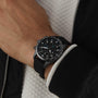A person wearing the IWC Schaffhausen Pilots Watch Performance Chronograph 41 Mercedes-AMG PETRONAS Formula One™ Team with a black dial and black rubber strap, paired with a black and white jacket.