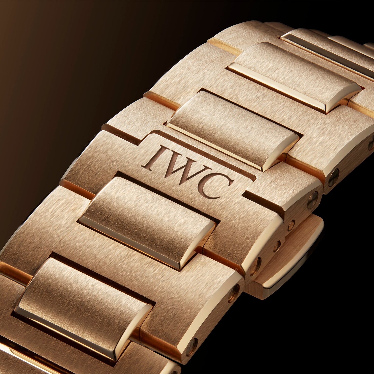 Close-up of the Ingenieur Automatic 40s 18-carat gold bracelet by IWC Schaffhausen, featuring an engraved link, set against a dark background.