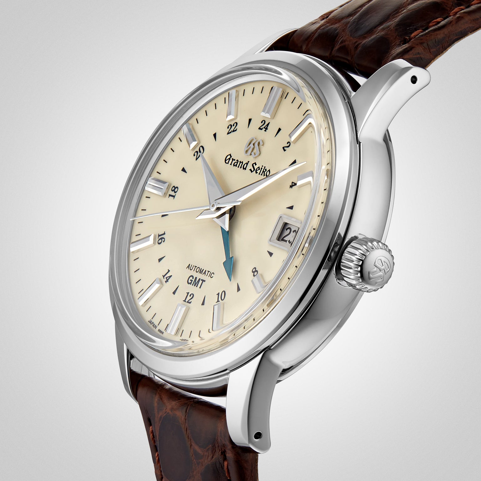 A Grand Seiko Automatic GMT Elegance wristwatch with a cream dial, silver markers, date window, and brown leather strap is displayed at an angle on a light background.