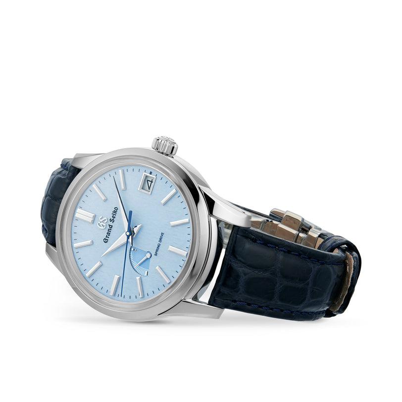 The Grand Seiko Spring Drive Elegance wristwatch features a light blue face, silver hour markers, date display, and a dark blue leather strap in an elegant stainless steel case, shown angled.