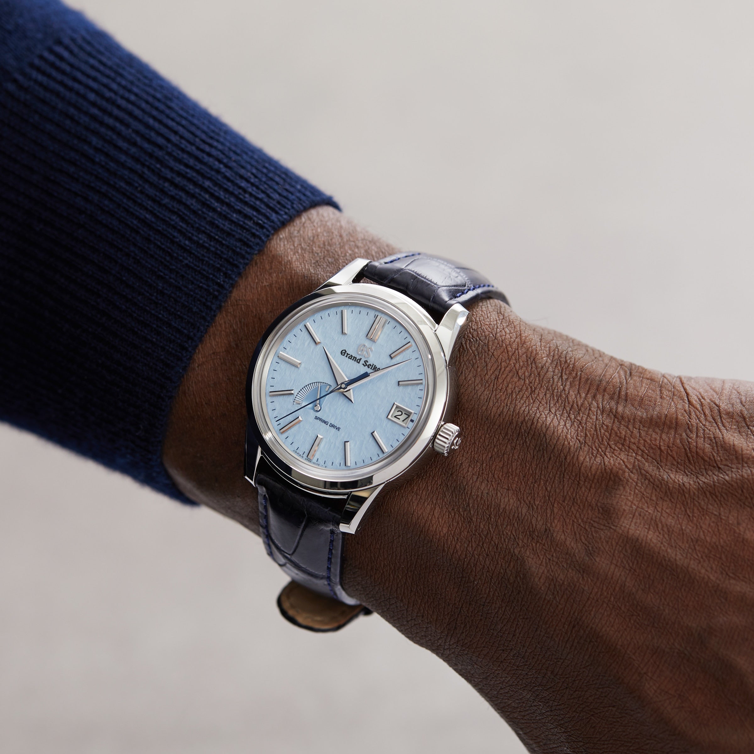 A person wearing the Grand Seiko Spring Drive Elegance, featuring a light blue face, leather strap, and stainless steel case, on their left wrist.