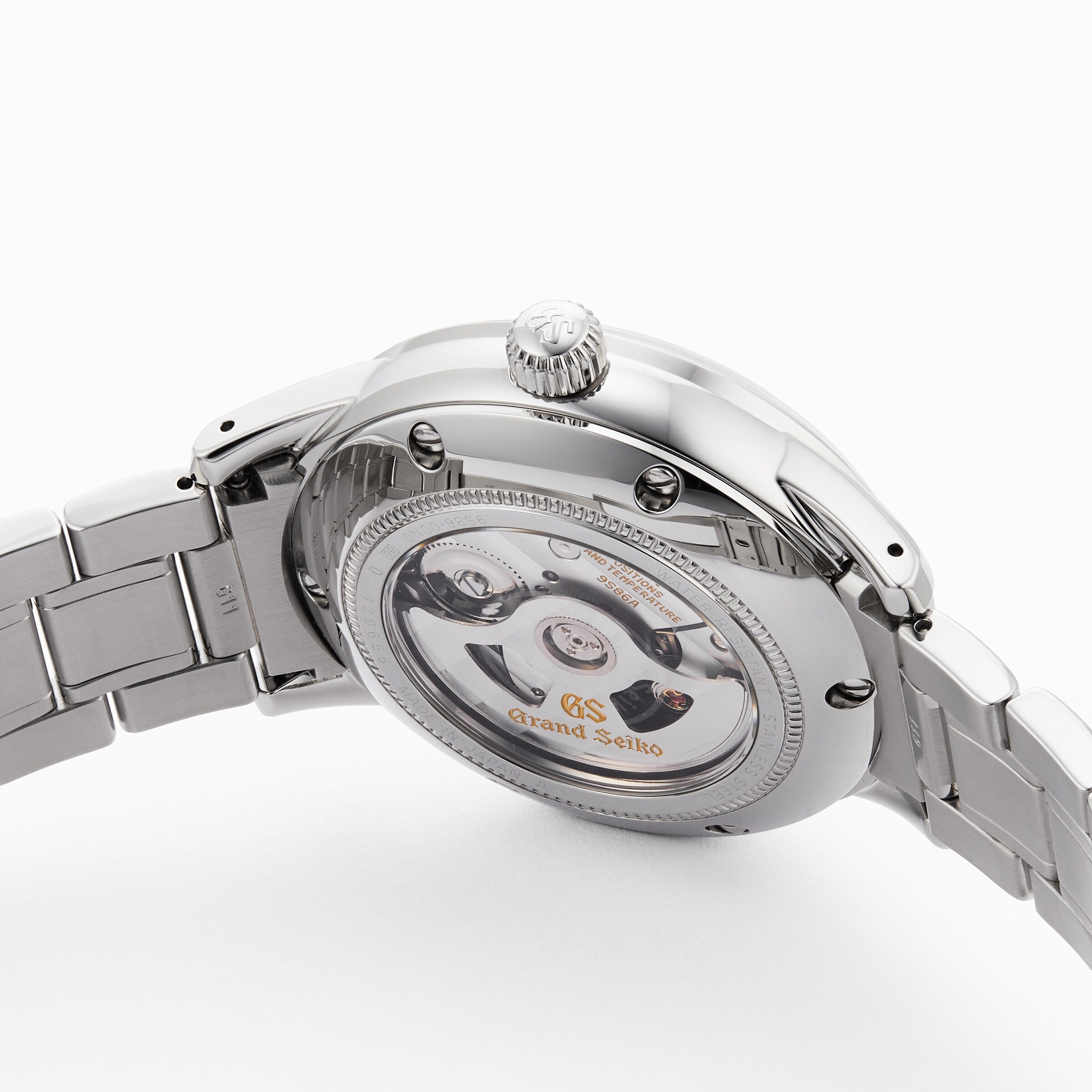 The image shows the back of a Grand Seiko Hi-Beat GMT Elegance watch with a stainless steel bracelet and a transparent case back displaying its automatic movement.